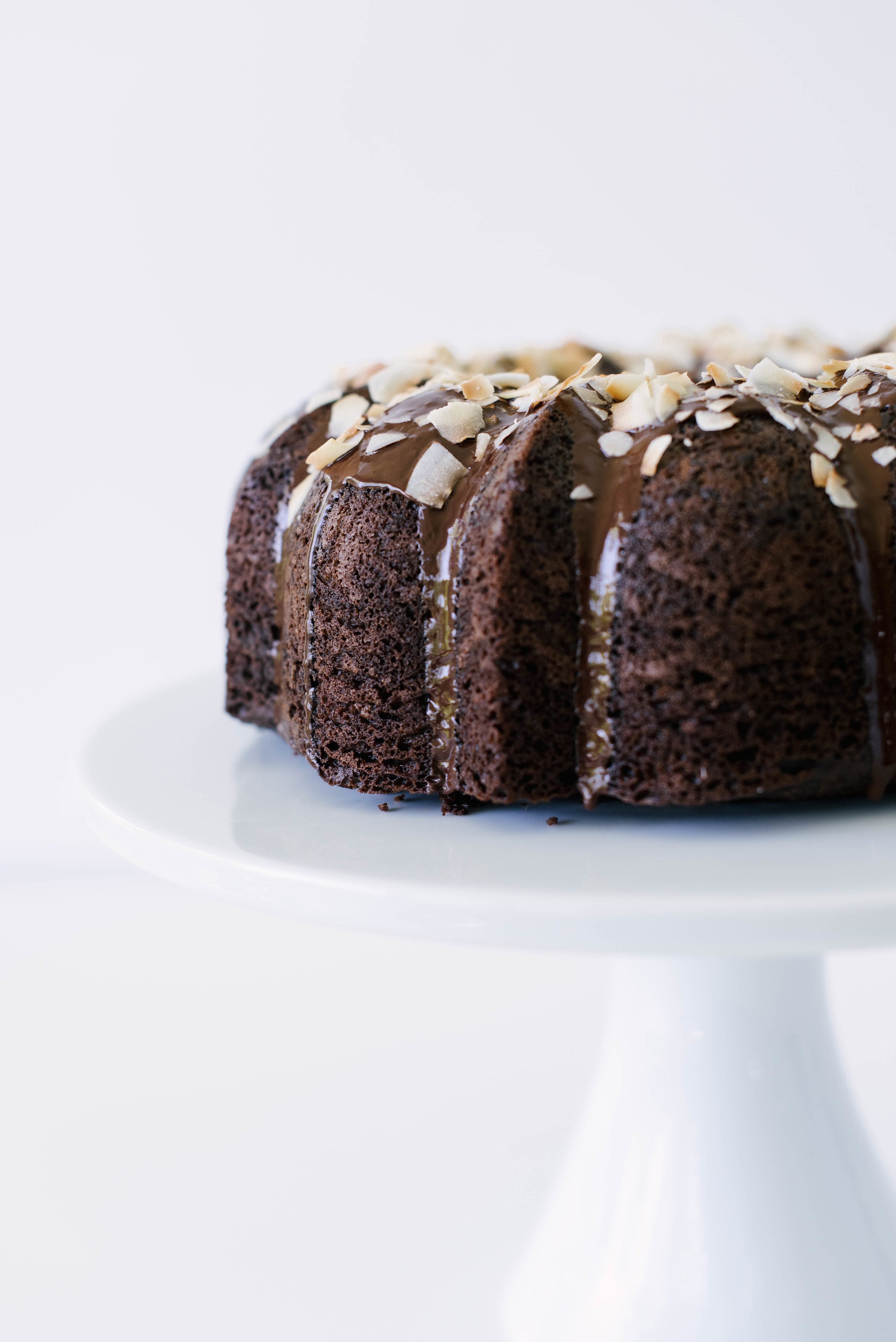 The side of Miss Jones Dark Chocolate Coconut Bundt Cake on a white cake stand