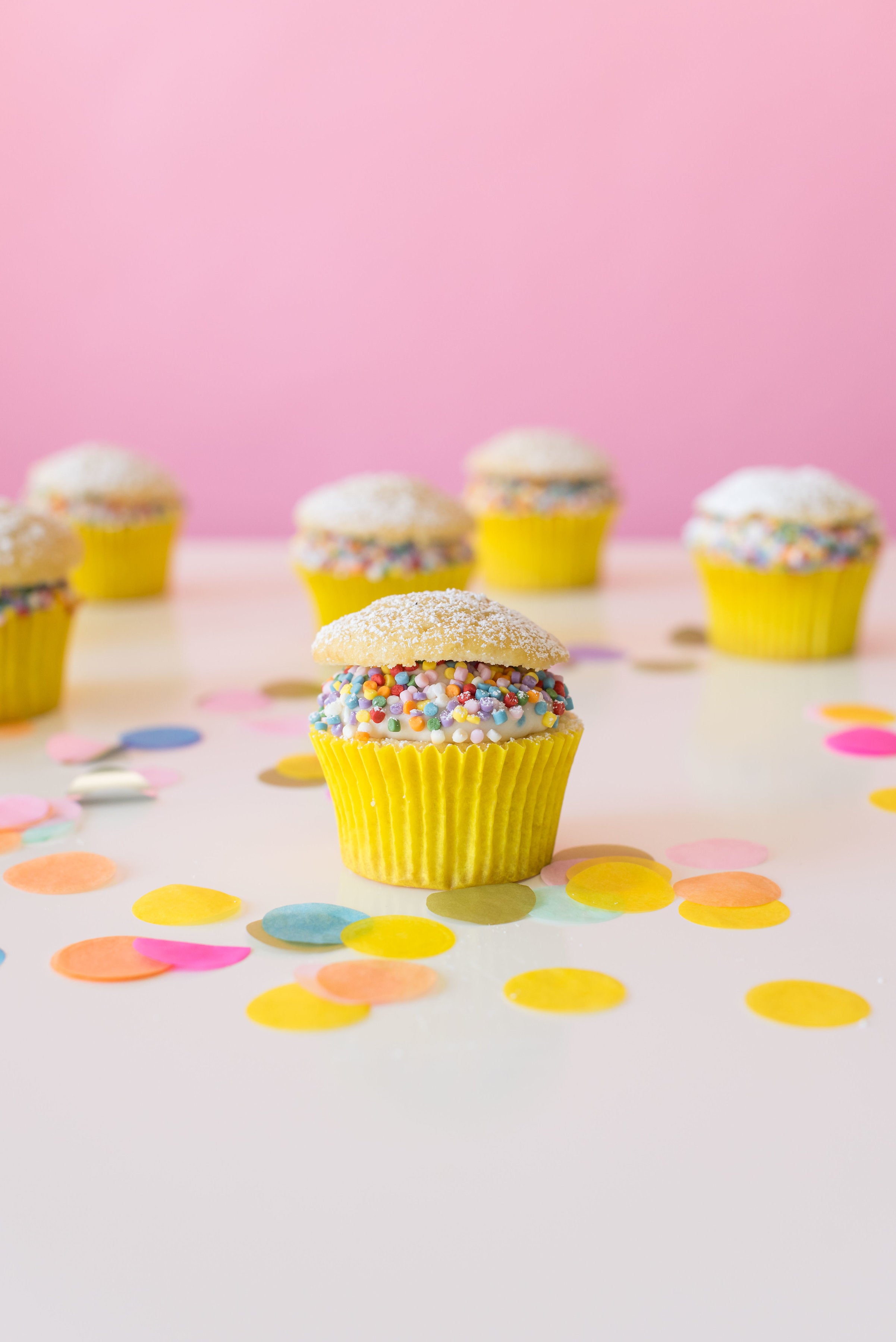 Image of side of six Miss Jones Baking Co Confetti Pop Cream Puff Cupcakes surrounded by confetti