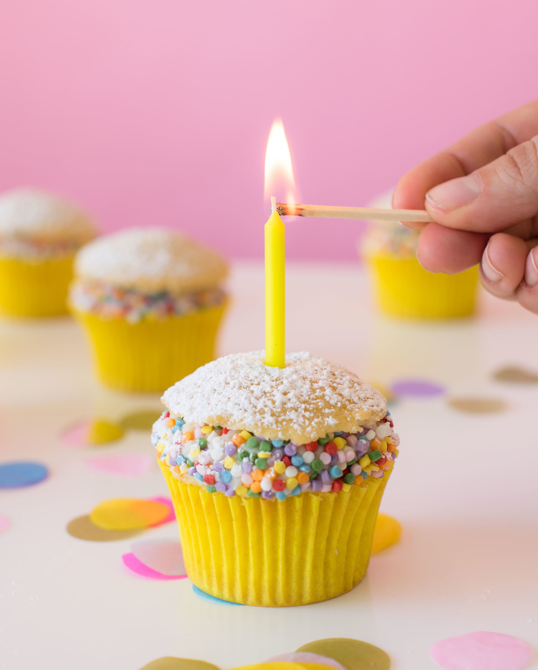 Image of side of Miss Jones Baking Co Confetti Pop Cream Puff Cupcake with a candle being lit