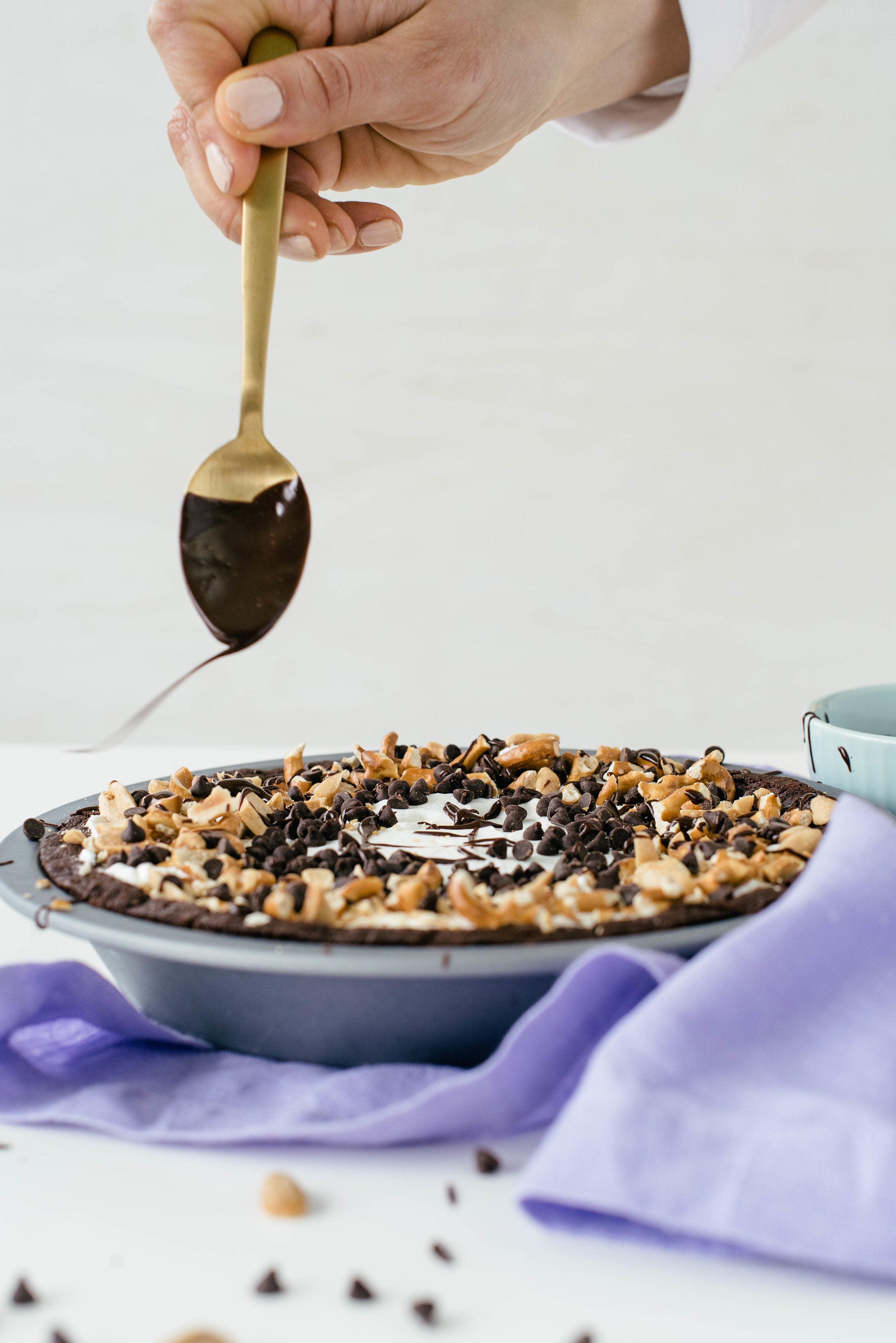 Image of a hand drizzling chocolate off a spoon onto Miss Jones Baking Co Salted Caramel Brownie Pie