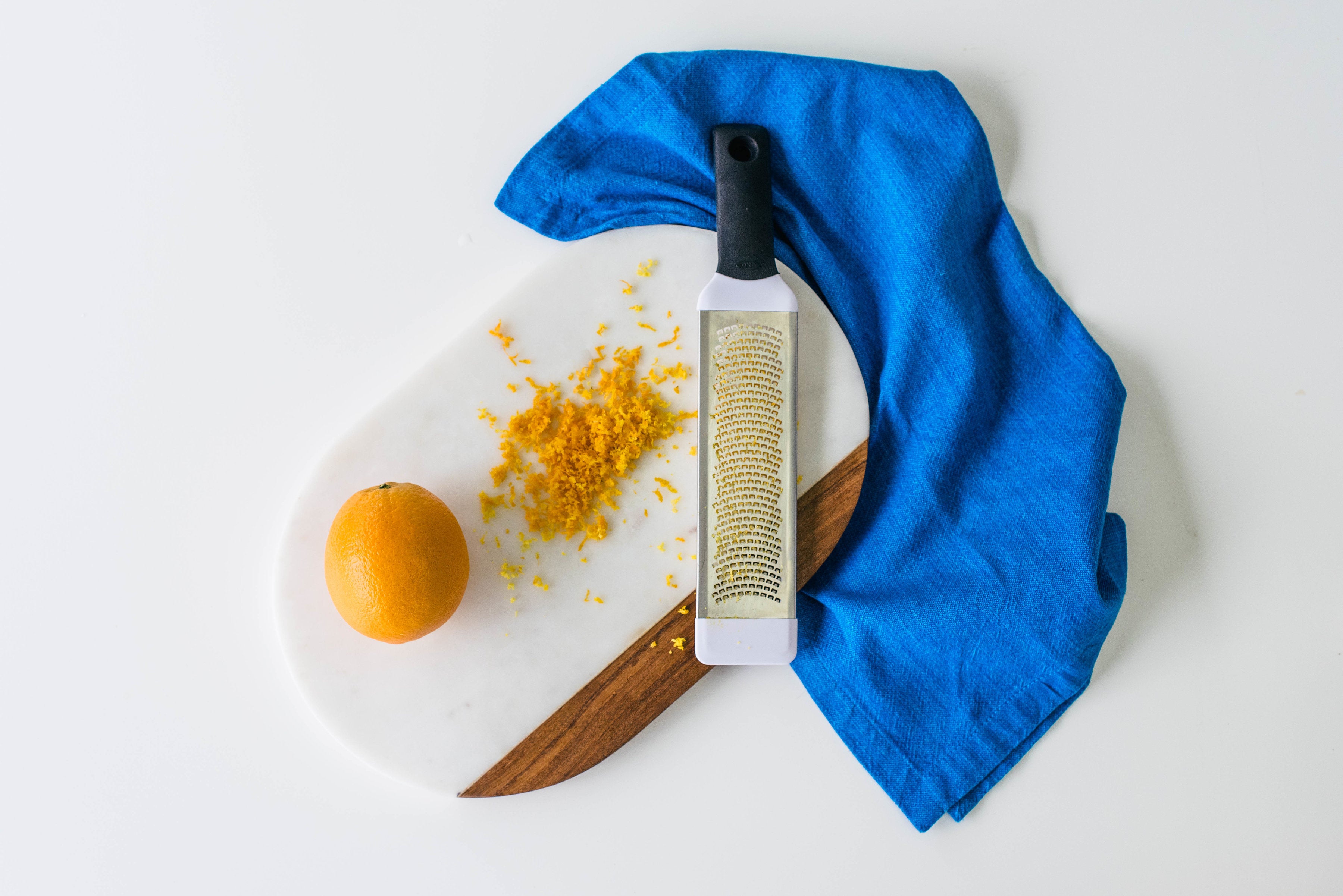 Image from above of an orange, orange zest, and a zester on a cutting board for Miss Jones Baking Co Mimosa Cupcakes