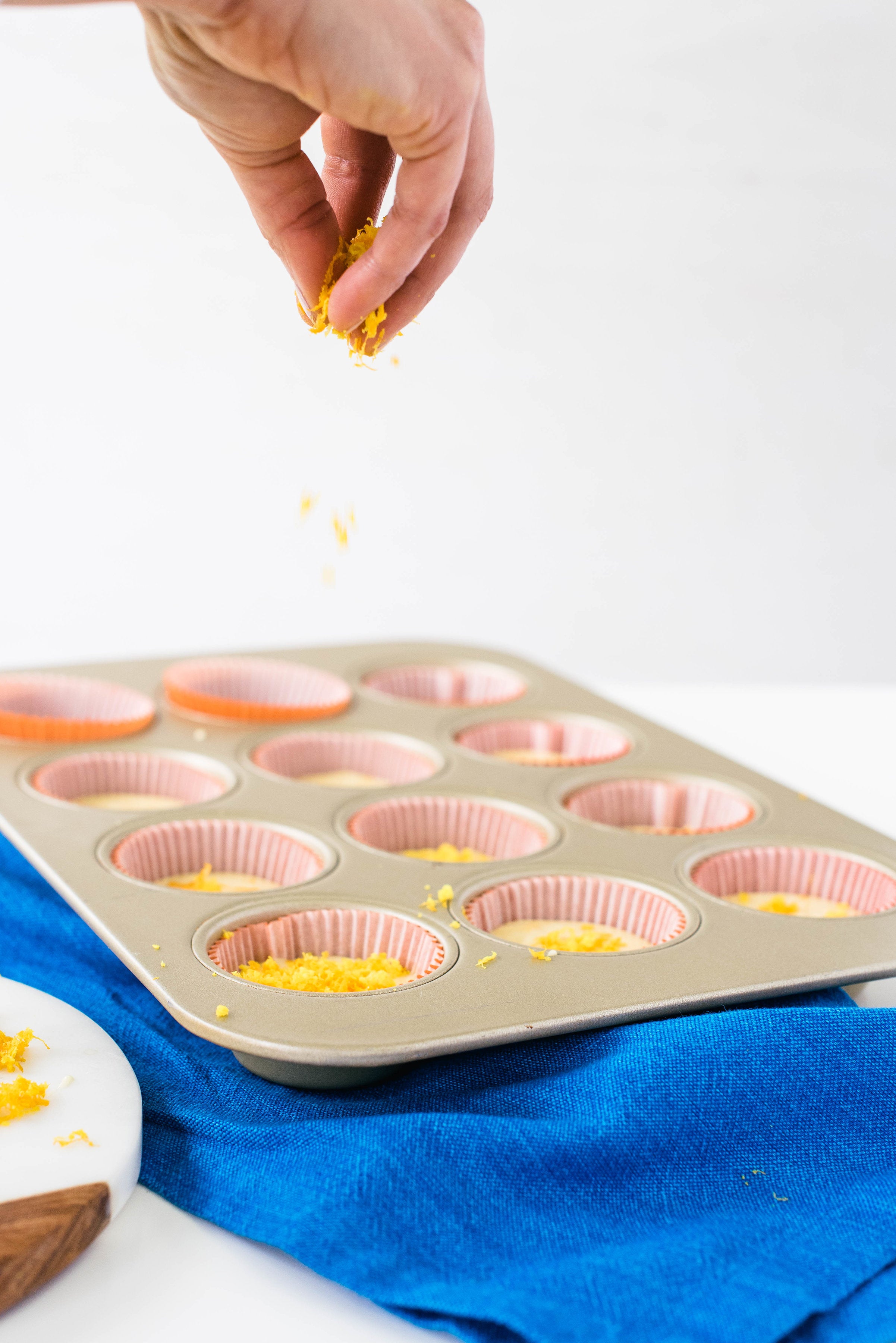 Image of a hand dropping orange zest onto Miss Jones Baking Co Mimosa Cupcakes batter in a cupcake pan