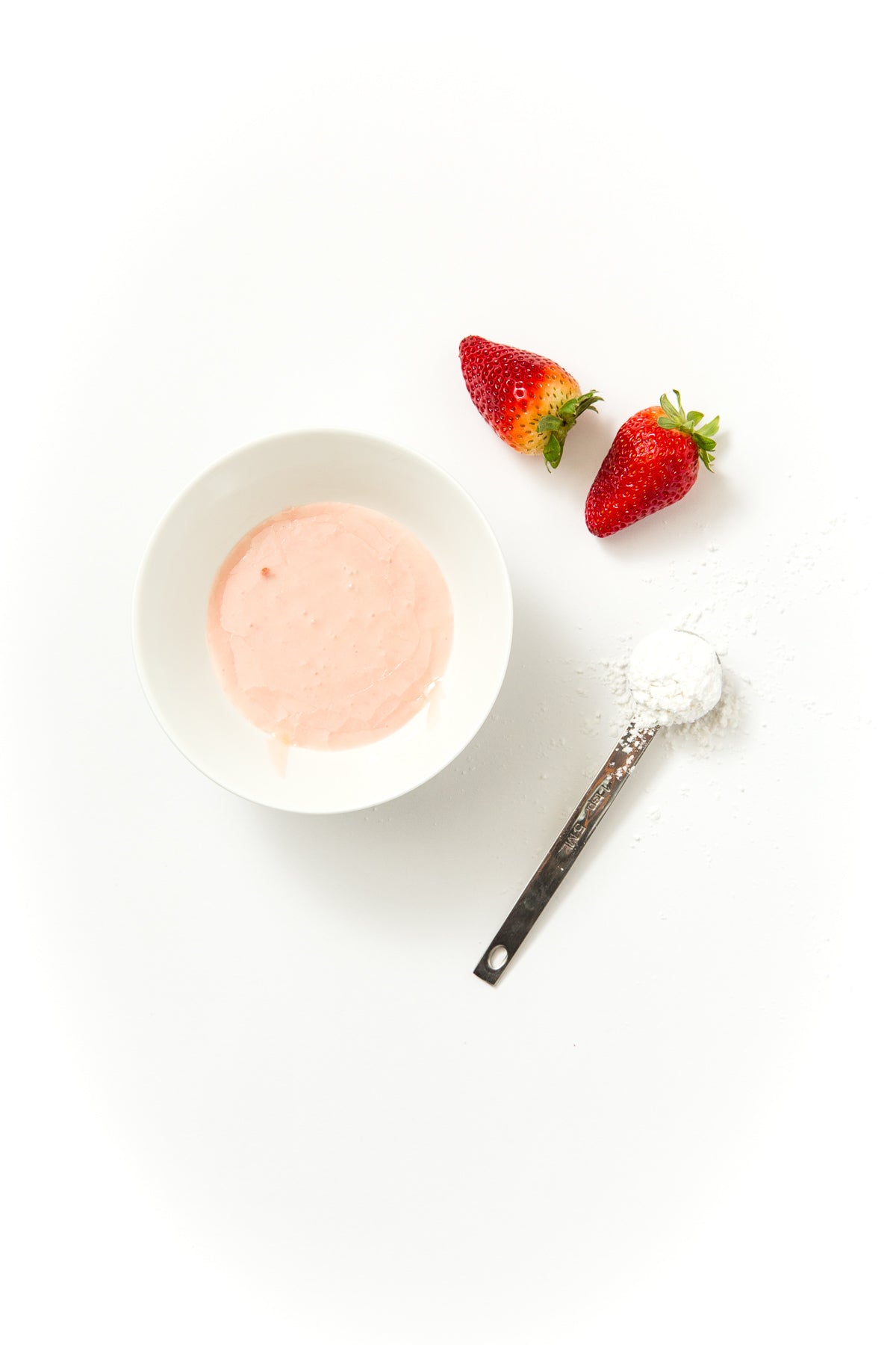 Image of a bowl of strawberry glaze next to two strawberries and a measuring spoon of powdered sugar for Miss Jones Baking Co Strawberry Buttermilk Donuts