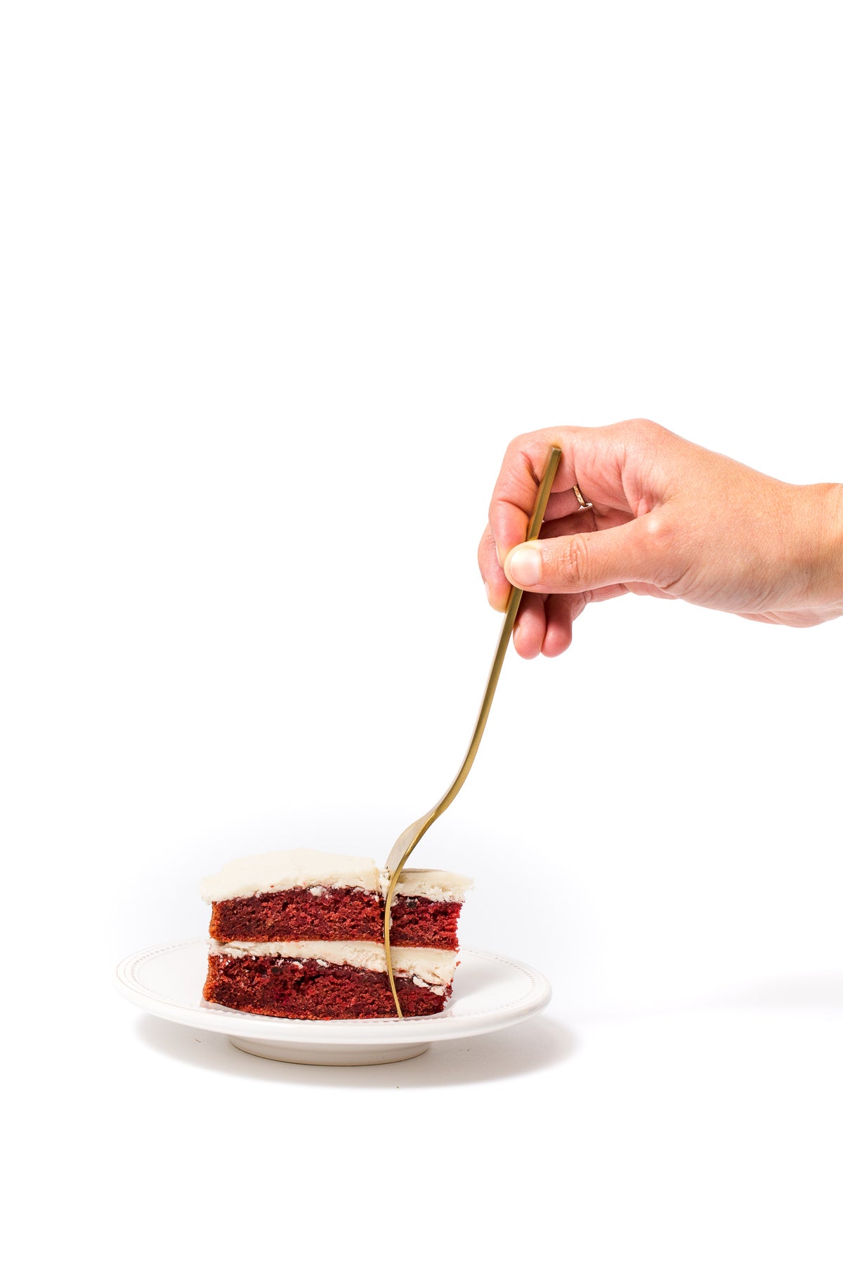 Image of slice of Miss Jones Baking Co Beet Red Velvet Layer Cake with a fork inserted into it by a hand