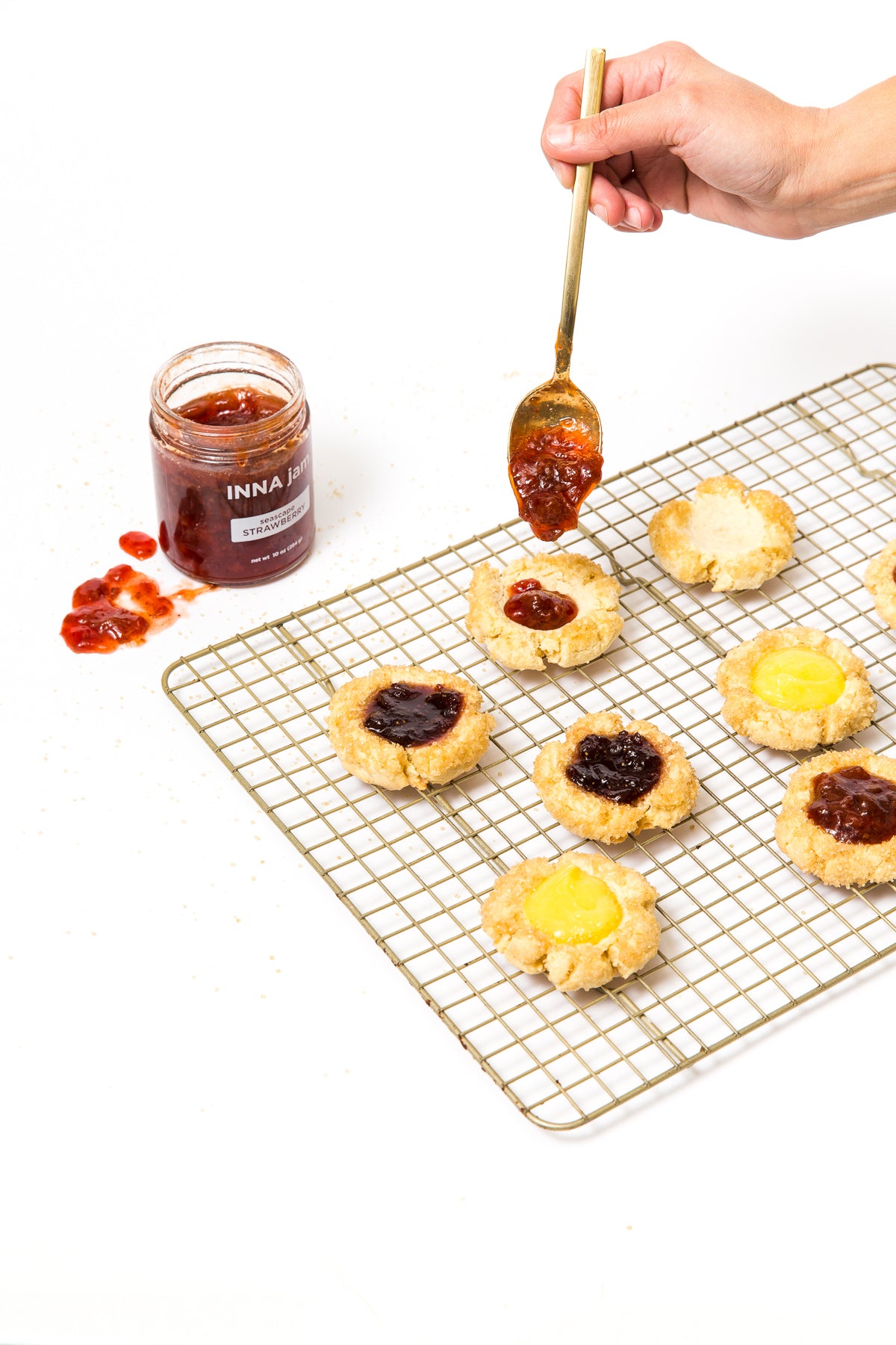 Image of baking rack with seven Miss Jones Baking Co Cake Batter Thumbprint Cookies being filled with jam filling. 