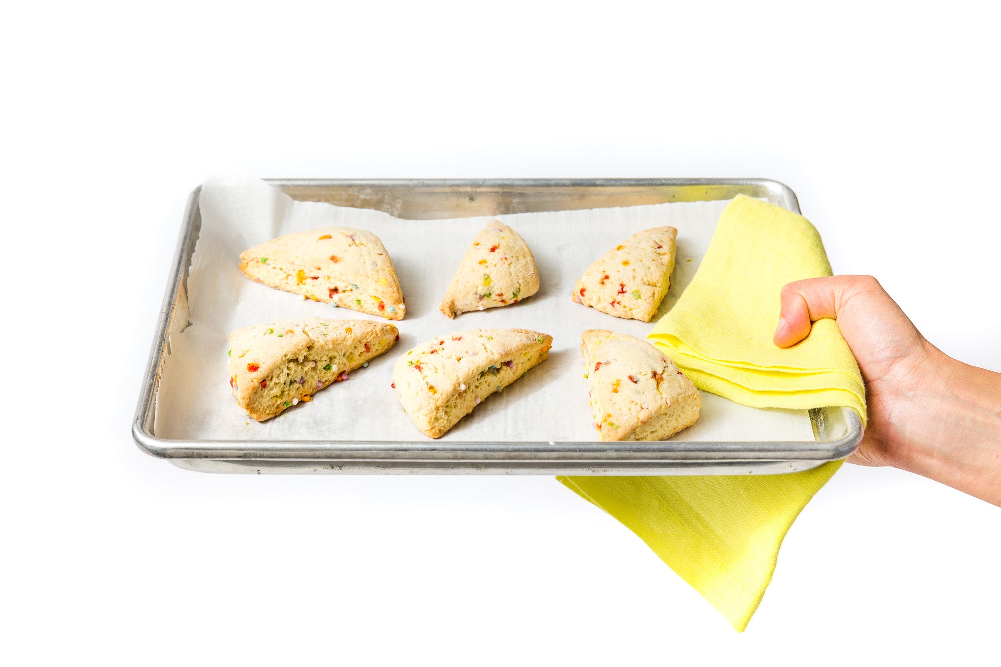 Image of a hand holding a baking sheet with six Miss Jones Baking Co Confetti Pop Cookie Mix Sprinkle Scones