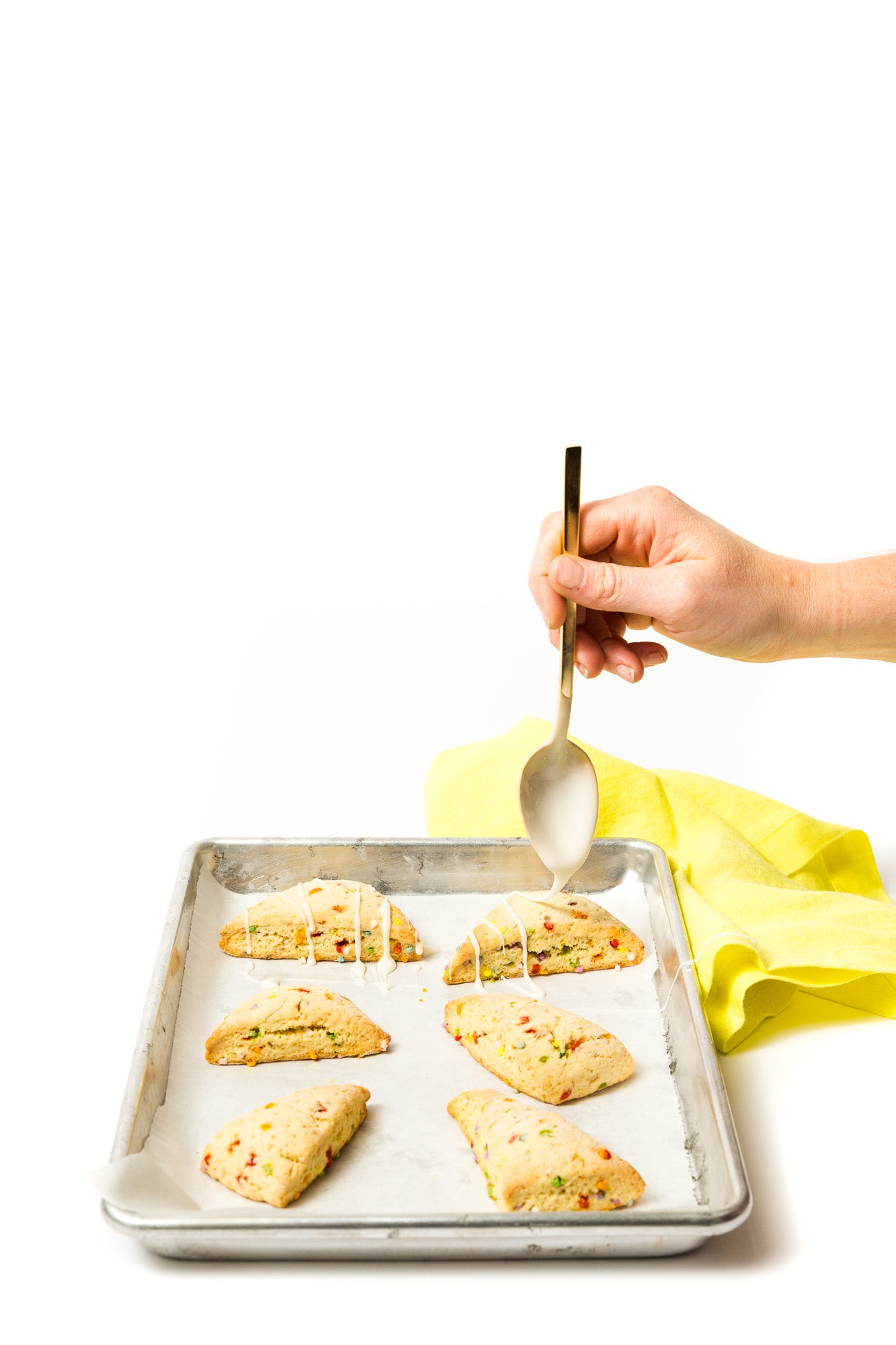 Image of hand glazing six Miss Jones Baking Co Confetti Pop Cookie Mix Sprinkle Scones on a baking sheet