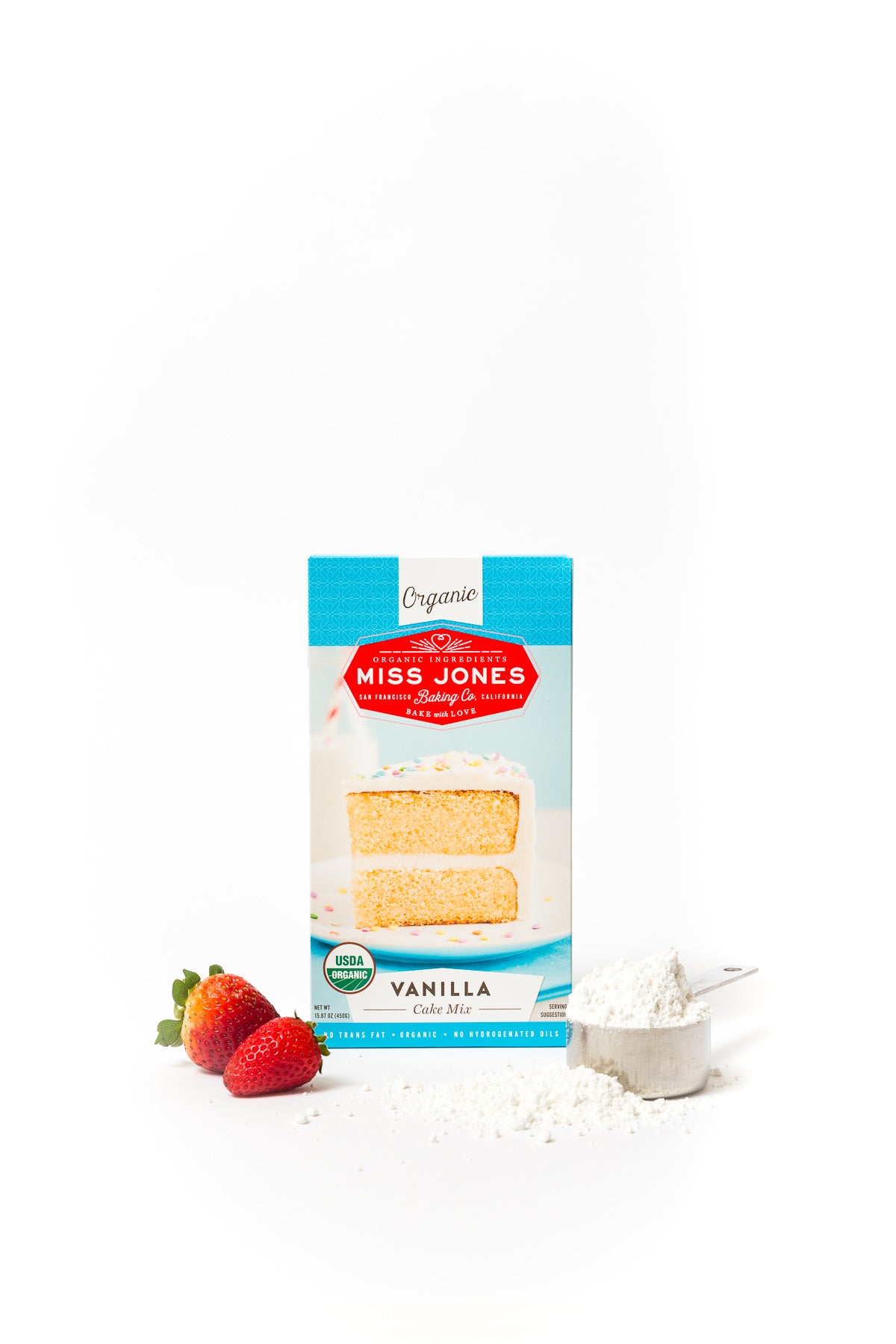 A box of Miss Jones Vanilla Cake Mix next to strawberries and a measuring cup of cake mix for Miss Jones Baking Co Strawberry Buttermilk Donuts recipe