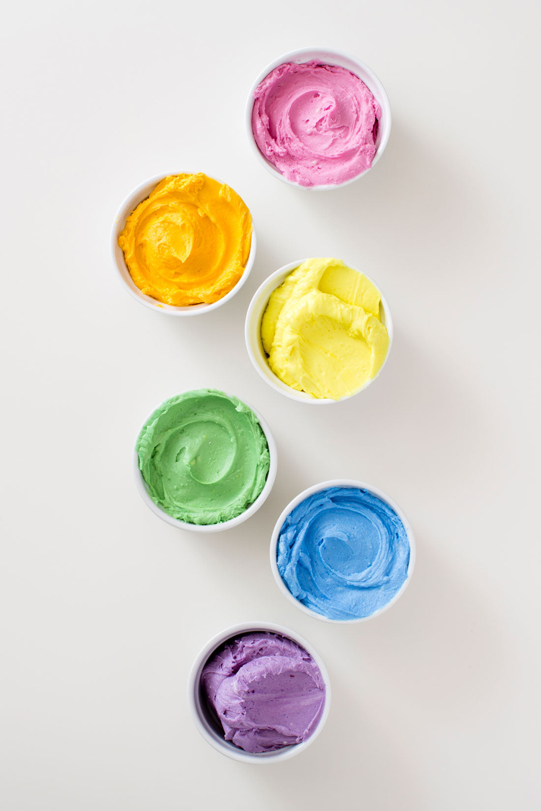 Image of pink, orange, yellow, green, blue, and purple frostings in bowls for Miss Jones Baking Co Naturally Dyed Rainbow Frosted Layer Cake