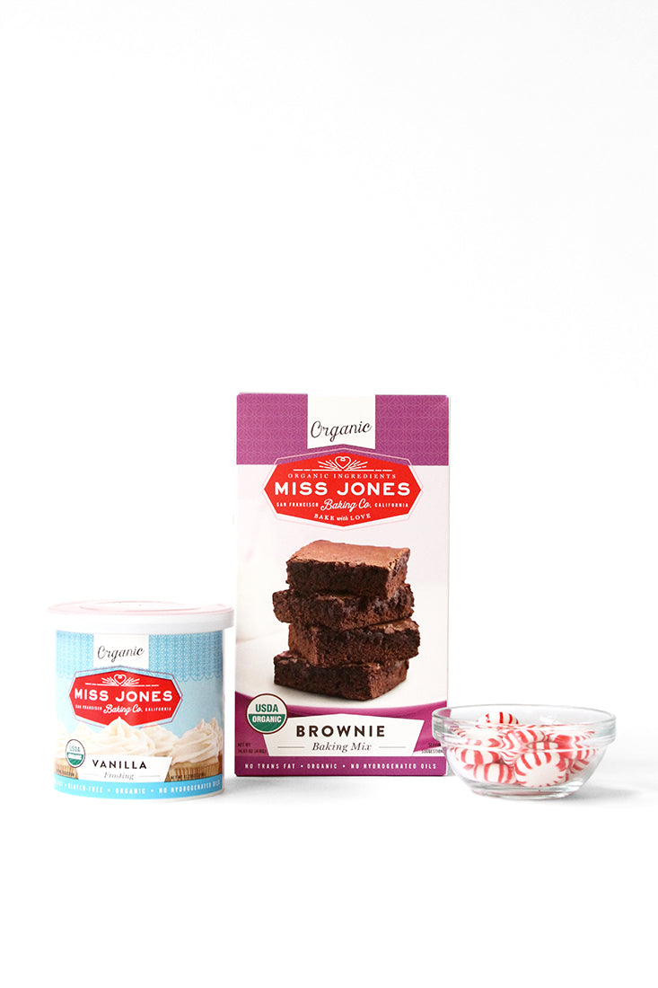 Image of a box of Miss Jones Brownie Mix, a jar of Miss Jones Vanilla Frosting, and peppermint candies in a bowl used in Miss Jones Baking Co Peppermint Bark Brownies Recipe