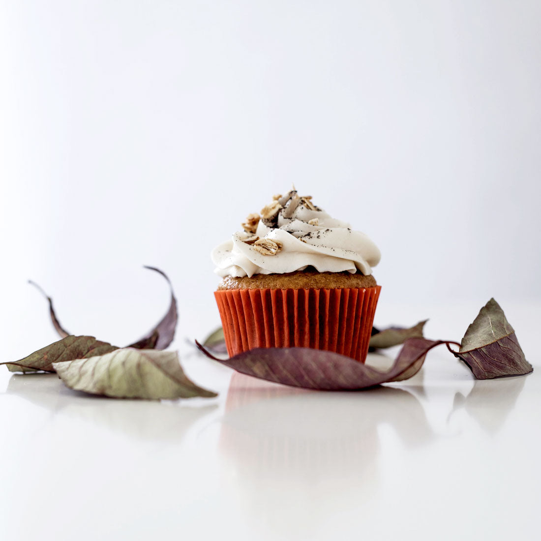 Image of the side of a Miss Jones Baking Co Pumpkin Spice Latte (PSL) Cupcake surrounded by dry leaves