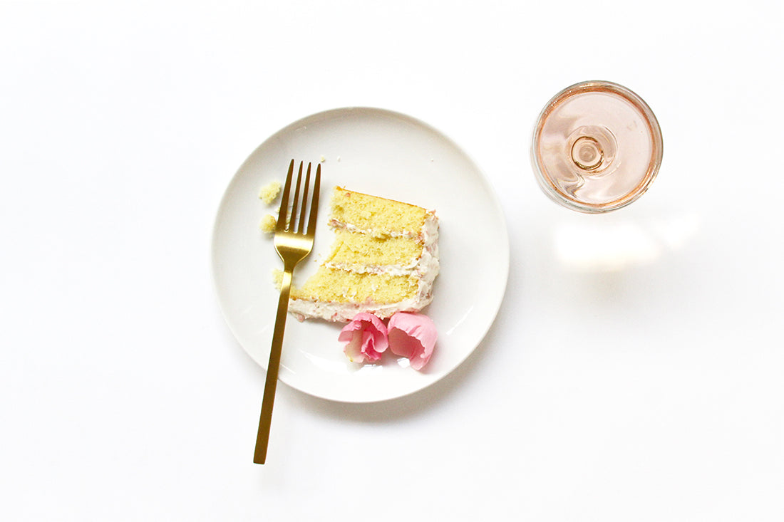 Image from above of a slice of Miss Jones Baking Co Rosé All Day Rose Cake on a plate next to a fork and a glass of rosé