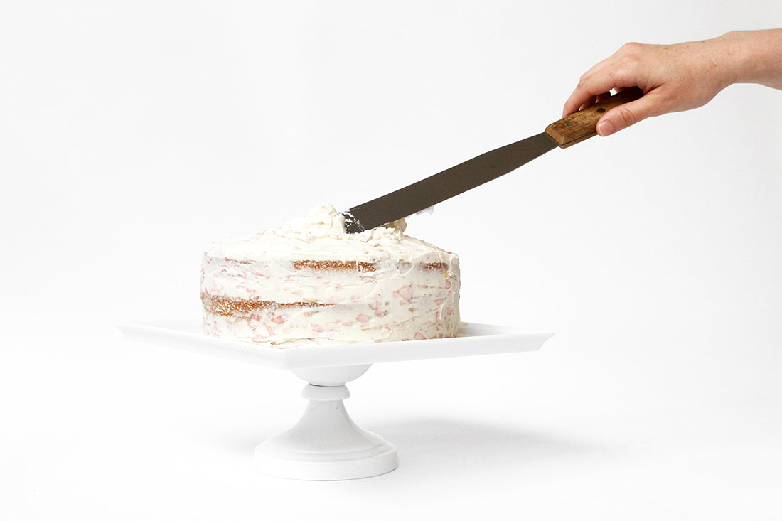 Image from the side of a hand frosting Miss Jones Baking Co Rosé All Day Rose Cake