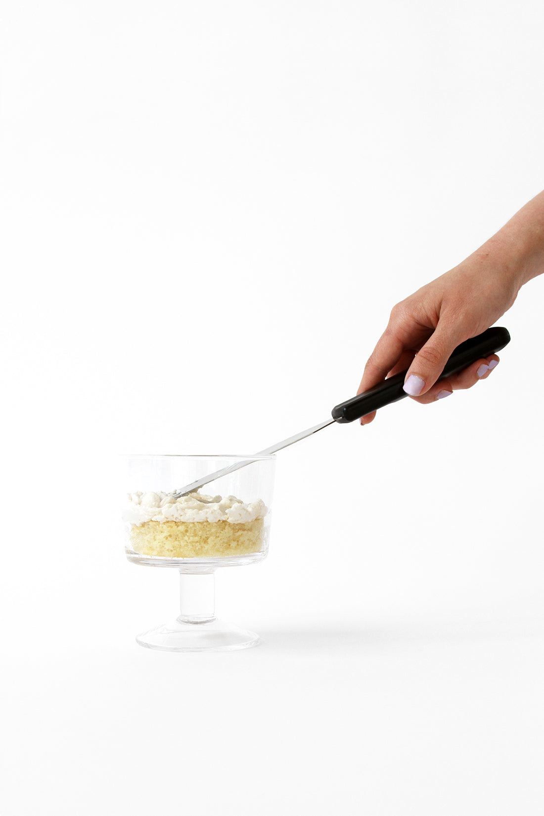 Image from the side of a knife spreading frosting over cake in a cup for Miss Jones Baking Co Stone Fruit Shortcake