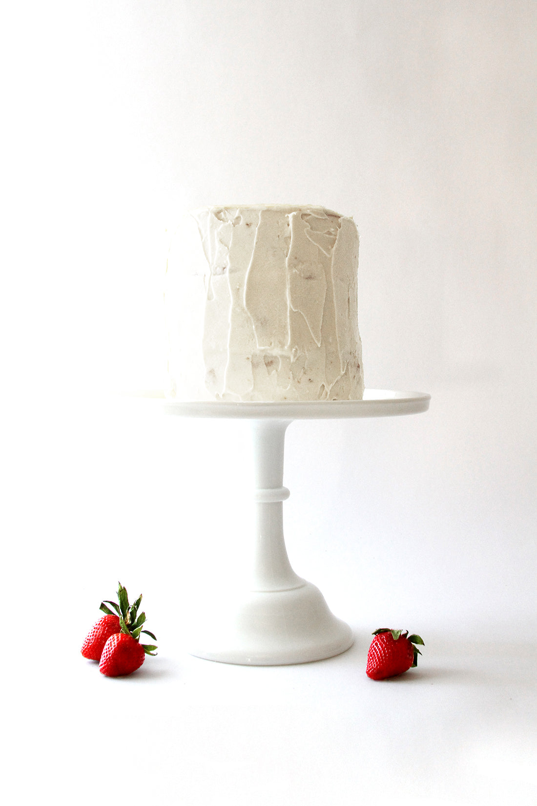 Image of cake stand with Miss Jones California Strawberry Cake on top and three strawberries surrounding the base of the stand.