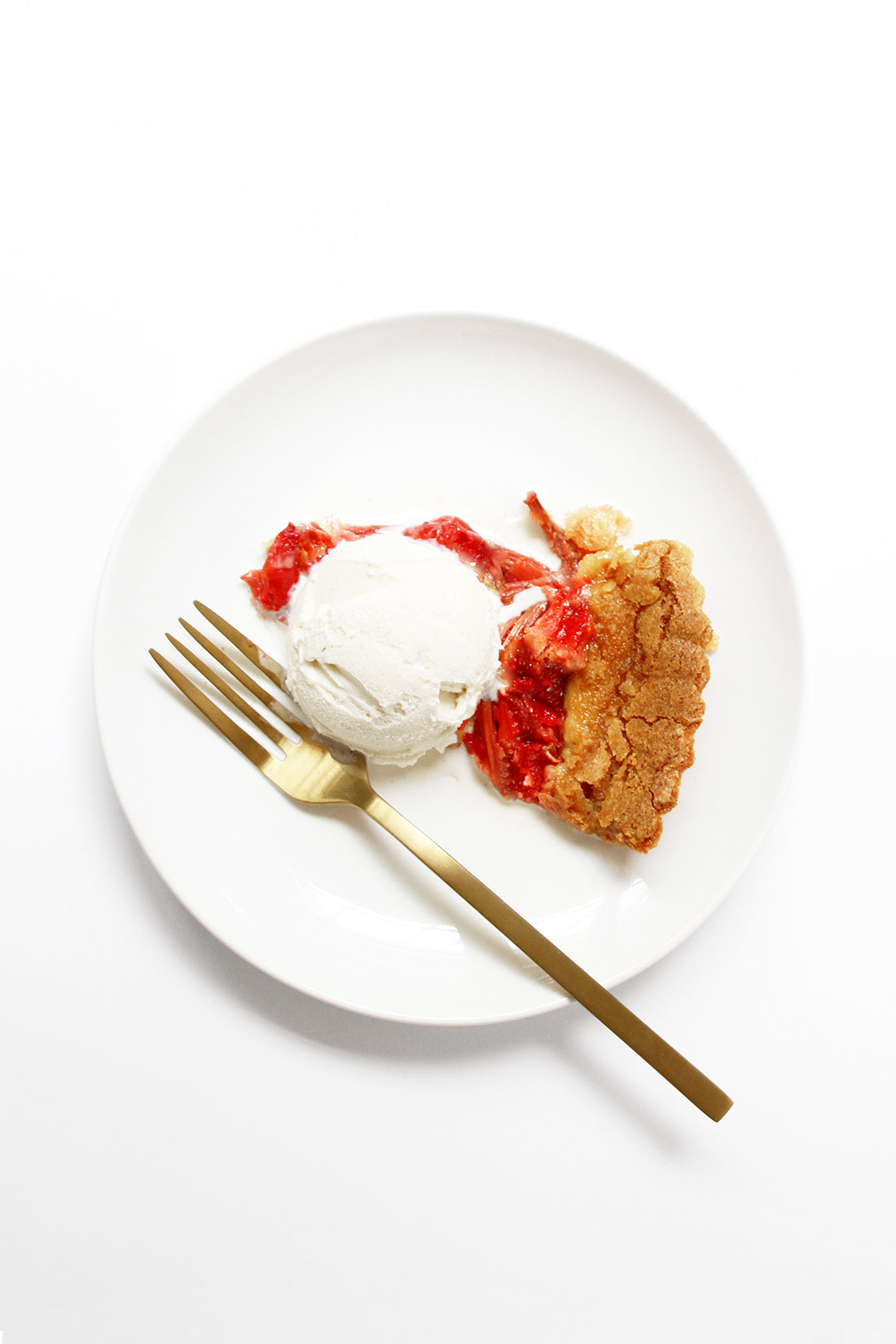 Image from above of a slice of Miss Jones Baking Co Summer Strawberry + Rhubarb Tart topped with vanilla ice cream next to a gold fork