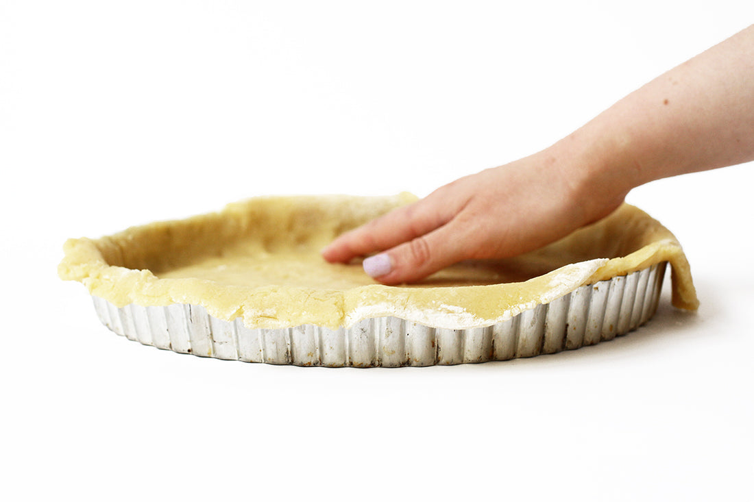 Image of the side of a hand pressing crust into a pie pan for Miss Jones Baking Co Summer Strawberry + Rhubarb Tart