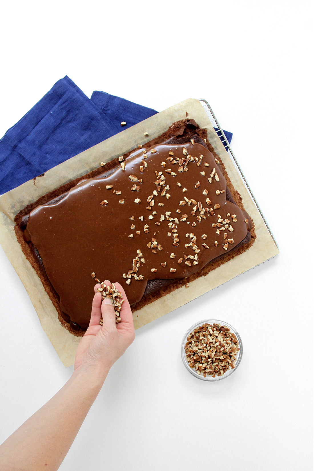 Image from above of a hand sprinkling chopped nuts onto Miss Jones Baking Co Sarah's Texas Sheet Cake