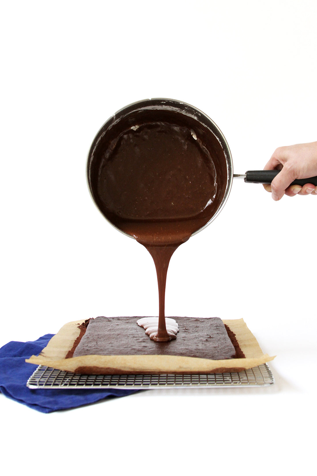 Image from the side of a hand pouring chocolate glaze onto Miss Jones Baking Co Sarah's Texas Sheet Cake on a baking rack
