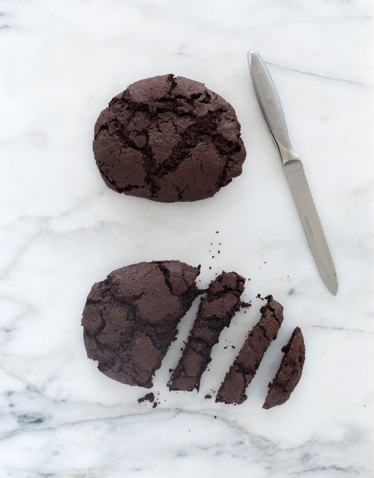 Image of top of two Miss Jones Baking Co Easy Chocolate Peppermint Cake Mix Biscotti cookies, one of which is partially cut into slices, on a marble counter next to a knife