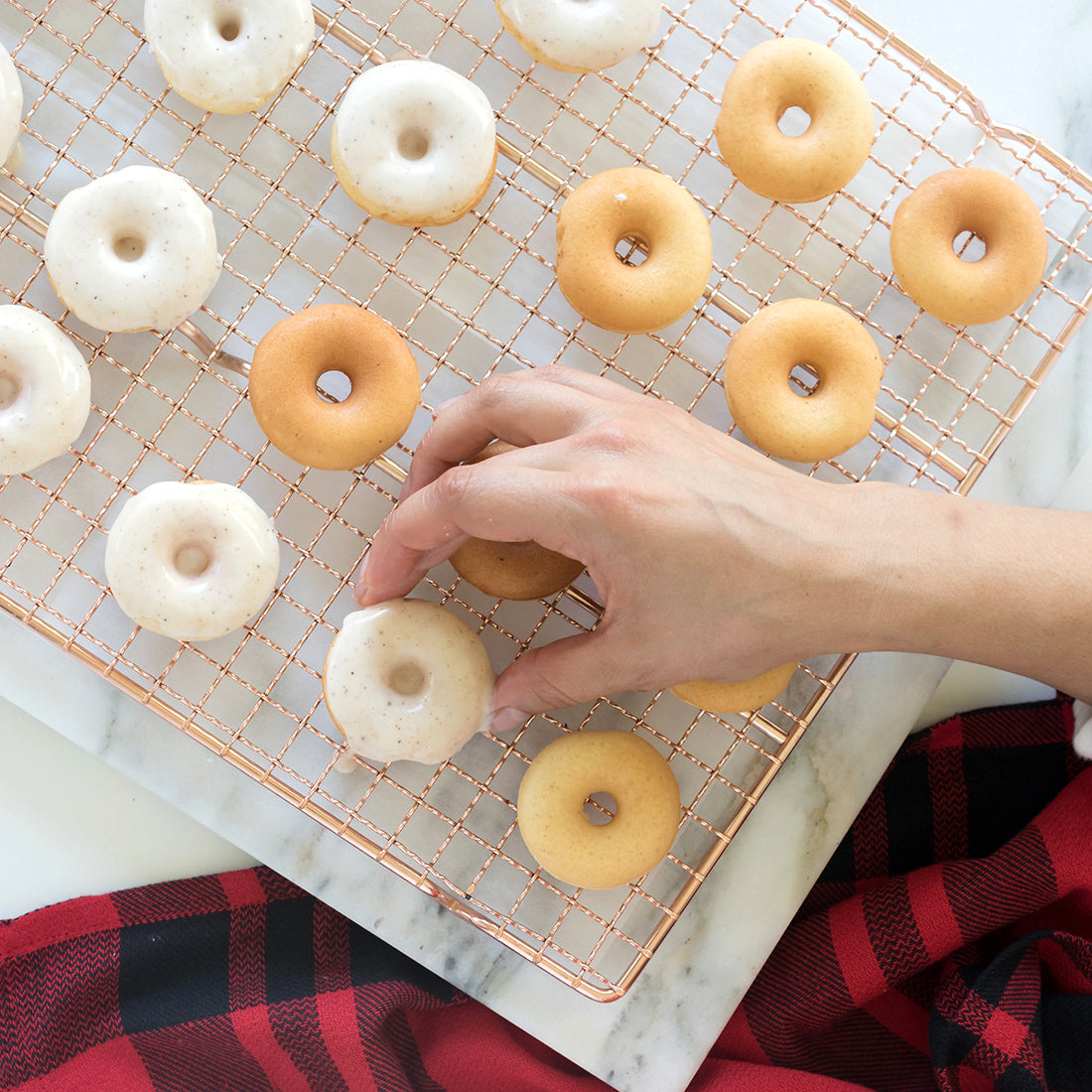 Image of a hand putting down glazed Miss Jones Baking Co Easy Holiday Eggnog Mini Donuts onto a copper baking rack