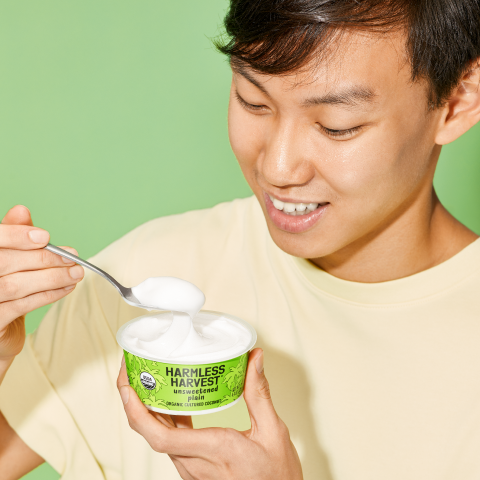 man holding harmless harvest dairy-free yogurt alternative and taking a spoonful out of it