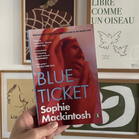 Blue Ticket by Sophie Mackintosh Book held in front of four prints available at Bellwoods