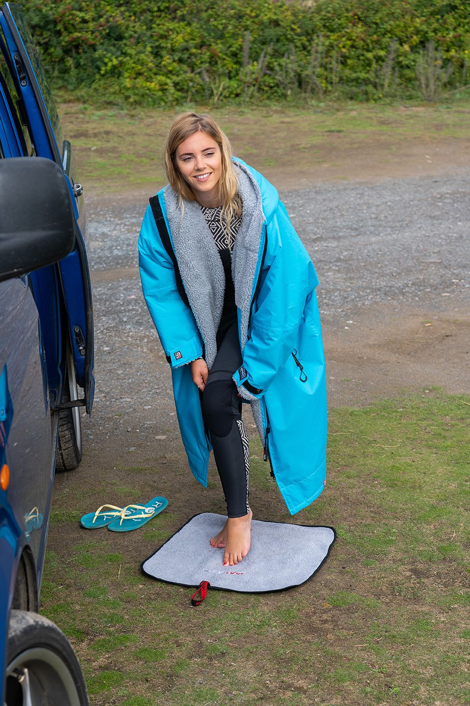 Woman standing on a Dryrobe changing mat while getting changed into a wetsuit.