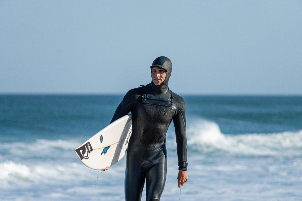 Man wearing the O'Neill Mutant Legend Wetsuit on the beach while carrying a surfboard 