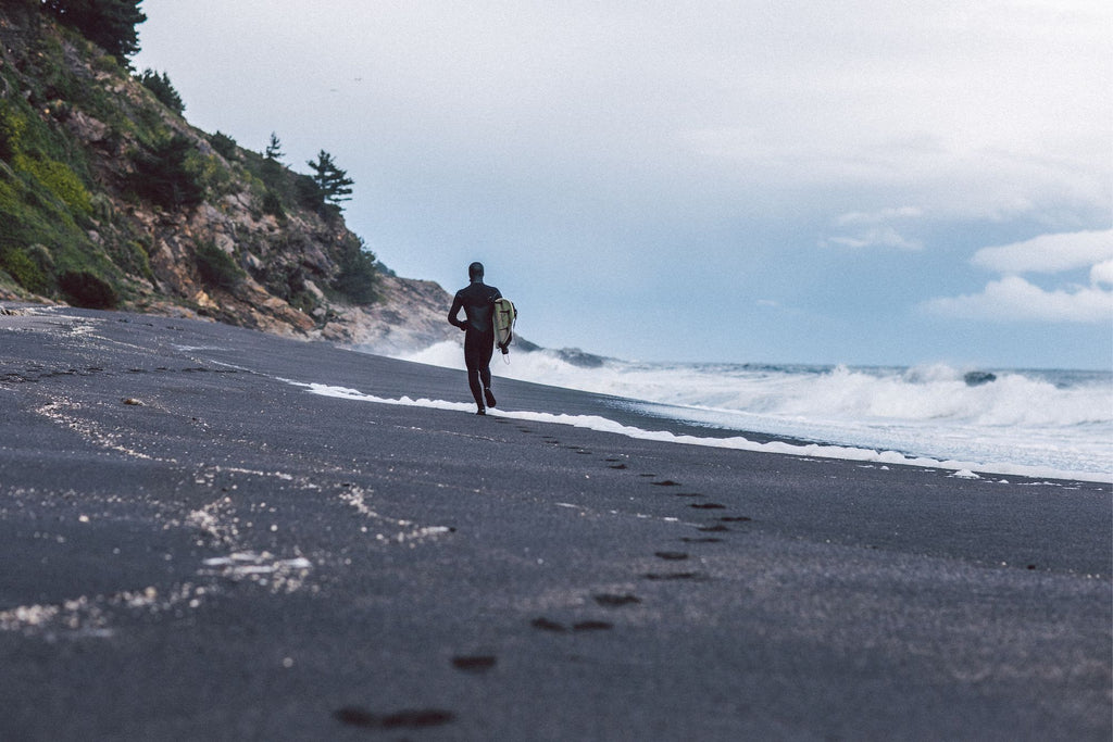 Man walking with his surfboard in the distance on the beach with waves crashing on the shore