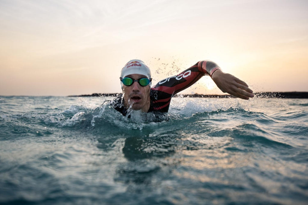 Man swimming in sea wearing Red Bull Swim Cap and Swim Goggles.