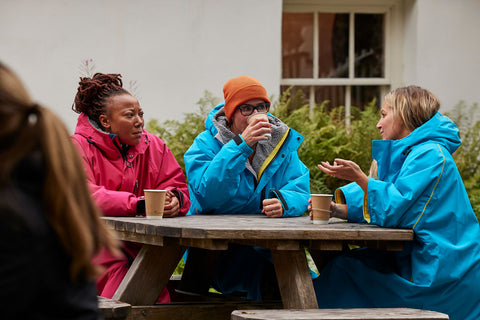 Women drinking coffee sitting at an outdoor table wearing their changing robes