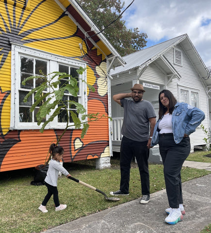 Anthony and his wife standing in front of a house with a mural on it. Their daughter Penelope is playing with a shovel.