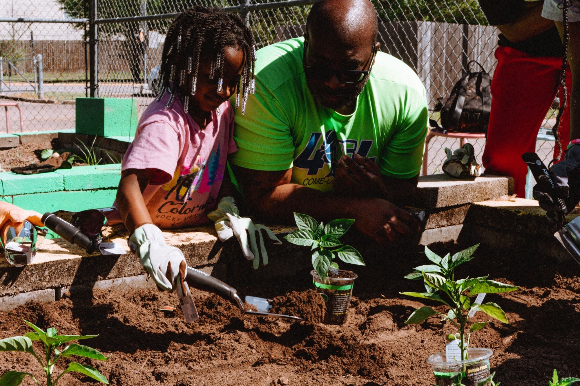 A father and his daughter work in the garden, both bent over the soil and examining a plant