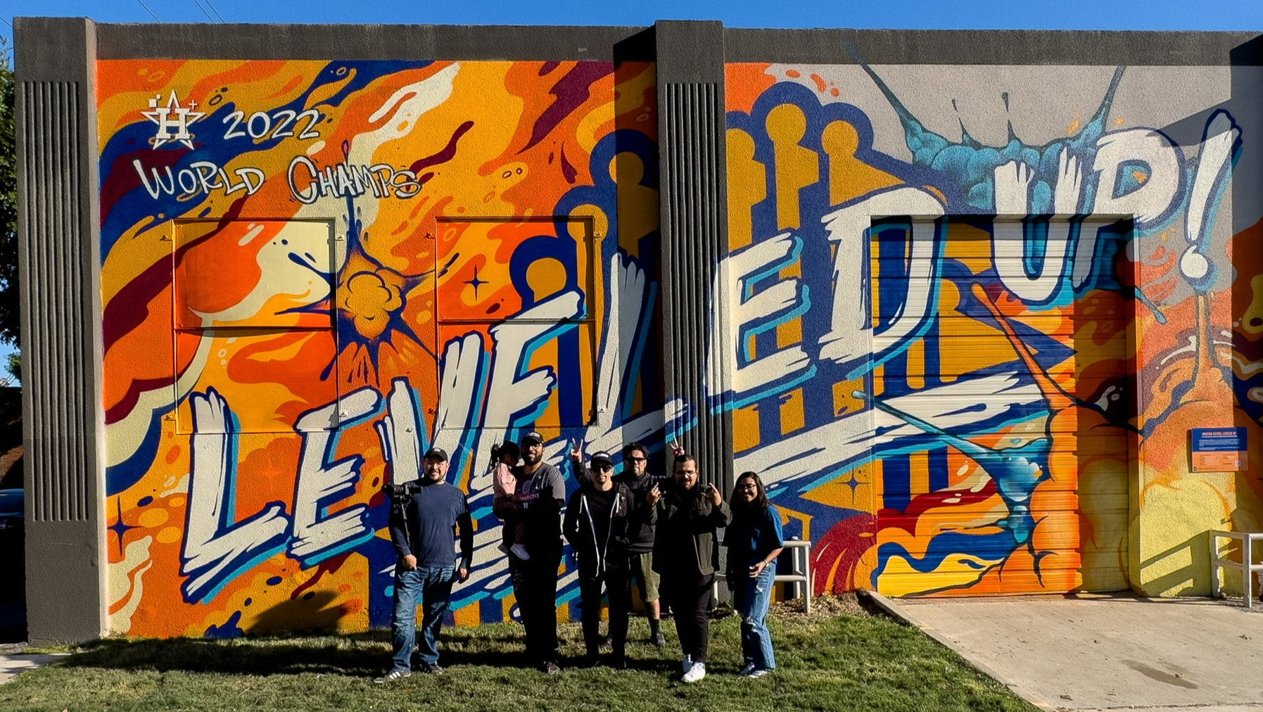 Anthony and his friends and family standing in front of a massive orange mural that reads "LEVELED UP!"
