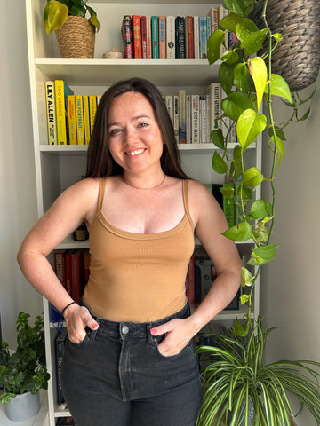 lady smiling wearing camel coloured vest top and black jeans