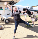 Lindsey jumping with her arms and legs in the air in front of a small plane.