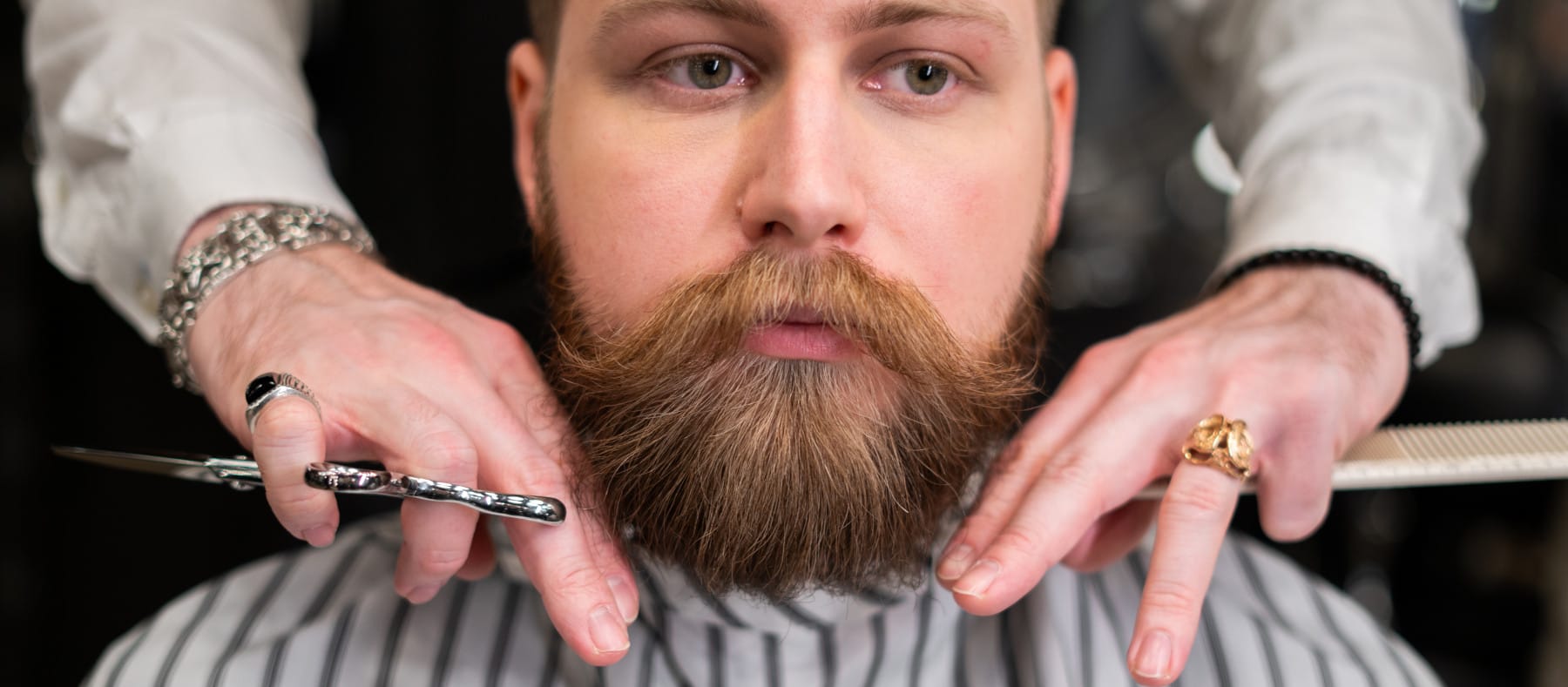 Man with pinstripe barber cape getting a beard cut