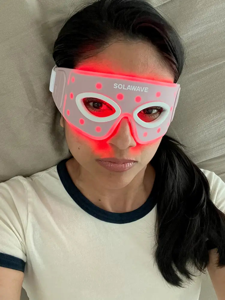 Person wearing a glowing red light therapy mask.