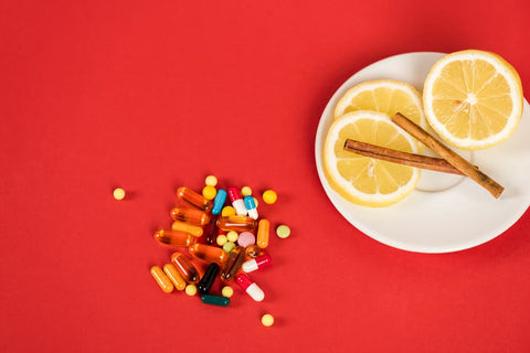 a colorful assortment of pills and capsules on a white plate alongside lemon slices and cinnamon sticks, suggesting a blend of traditional and natural immune-boosting options against a vibrant red background