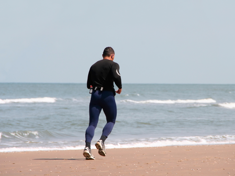 Man trägt lange Kleidung zum Schutz vor Sonnenallergie beim Joggen am Strand