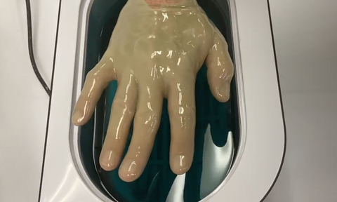 Man dipping hand in paraffin wax bath