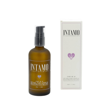 glass brown bottle of intamo start me up massage oil. Product is displayed with white box to the right centered in the middle of solid white background.