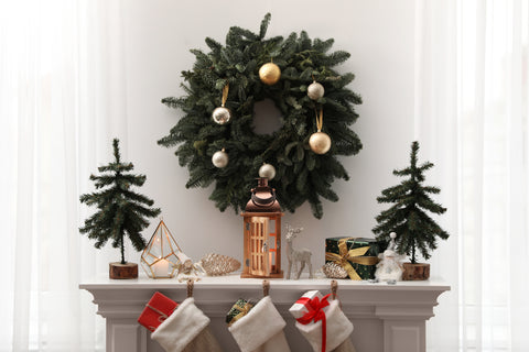 Several festive shaped ornaments scattered over mantel with small Christmas trees either side