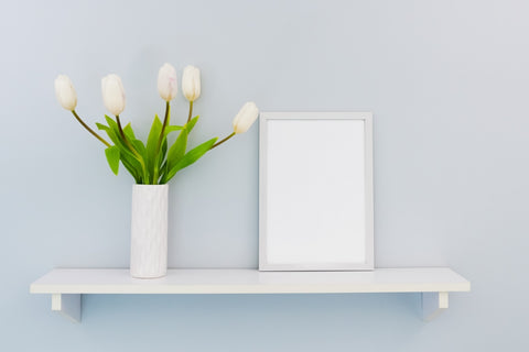 Simple shelving arrangement with white flower vase and white picture frame separated within a duck egg coloured background  