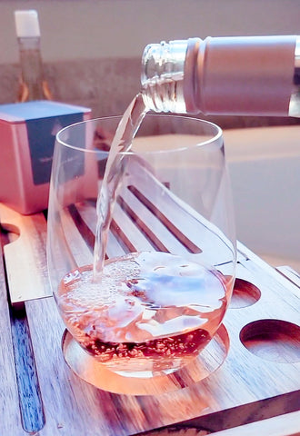 Pouring wine into glass during a bath soak.