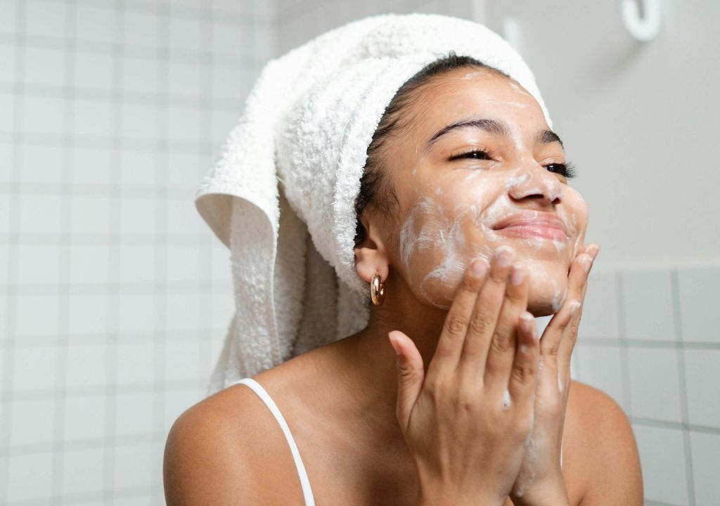 teenage girl washing her face in a white tiled bathroom