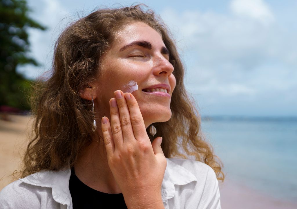 lady at the beach putting sunscreen on her face