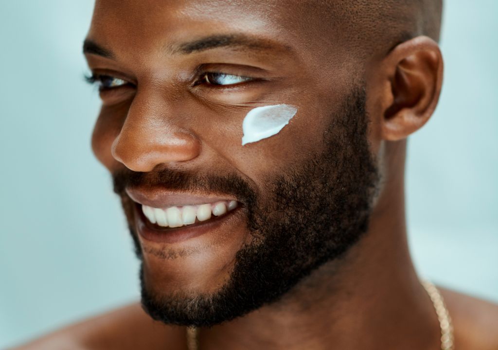 happy man with black skin applying sunscreen to his face