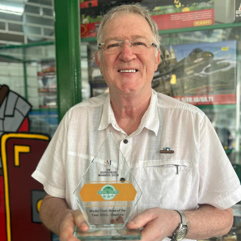 Paul Boyland, owner of Chester Model Centre, in white shirt stood in front of shop window holding a glass diamond shaped trophy for SME News UK Enterprise Awards 2023 Model Train Store of the Year Cheshire